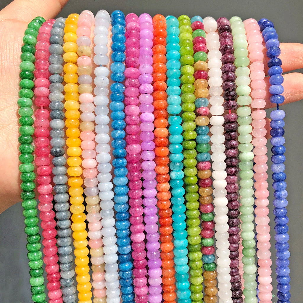 Hand holding multiple strands of multicolored natural stone flat round beads