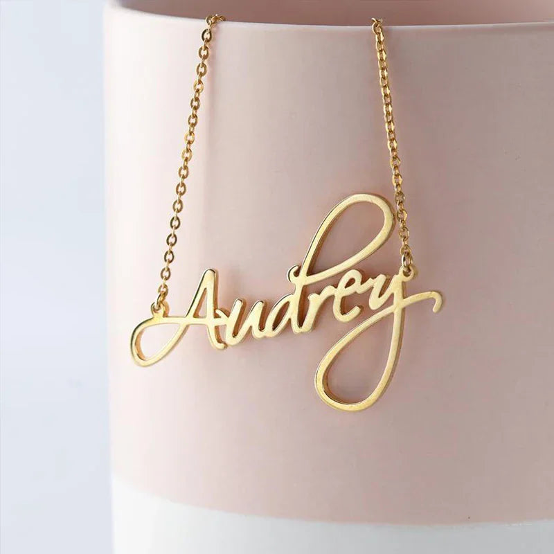 Gold custom script name necklace hanging on a pink vase