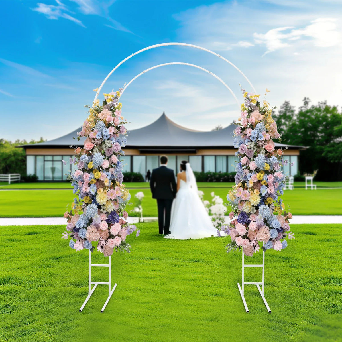 White metal round arch frame decorated with colorful flowers on a garden lawn in front of a building