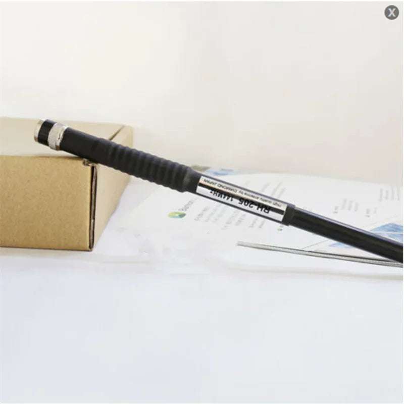 A black telescopic antenna with BNC connector next to a cardboard box.