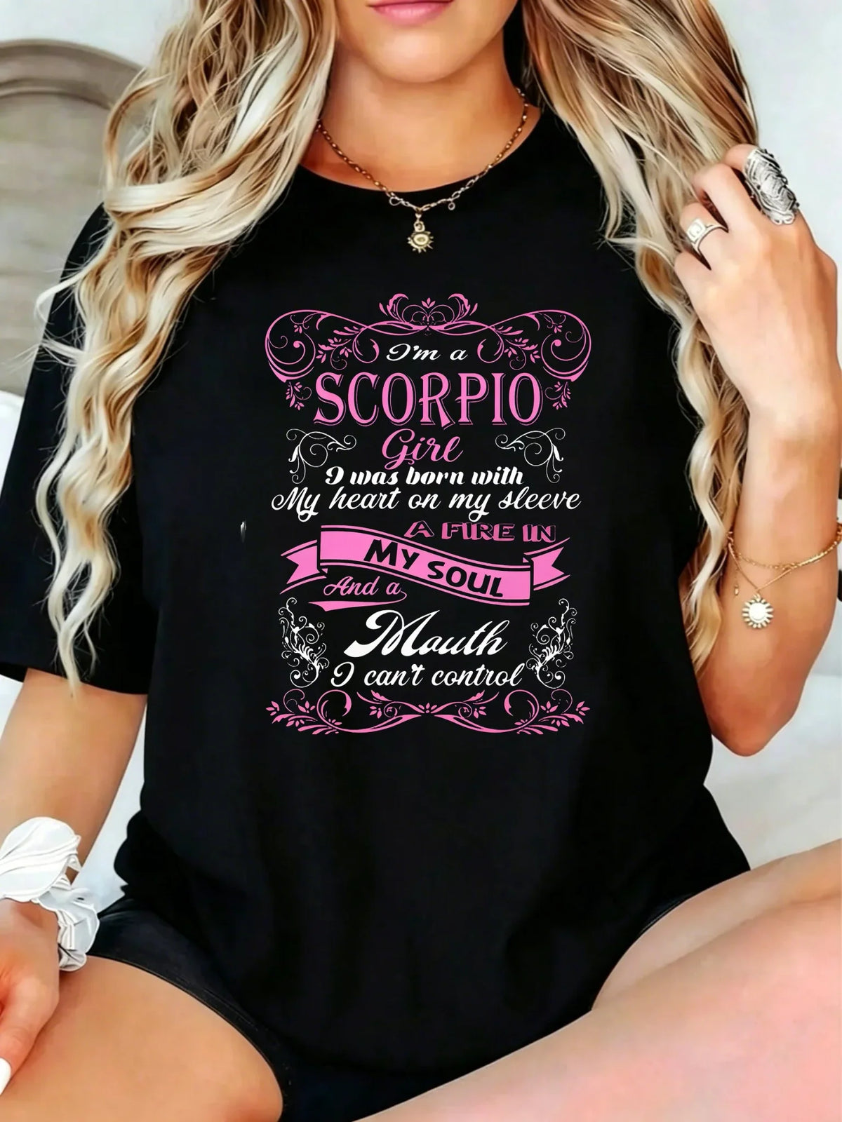 Black short-sleeve t-shirt with pink and white Scorpio zodiac graphic print, worn by a woman with long blonde hair