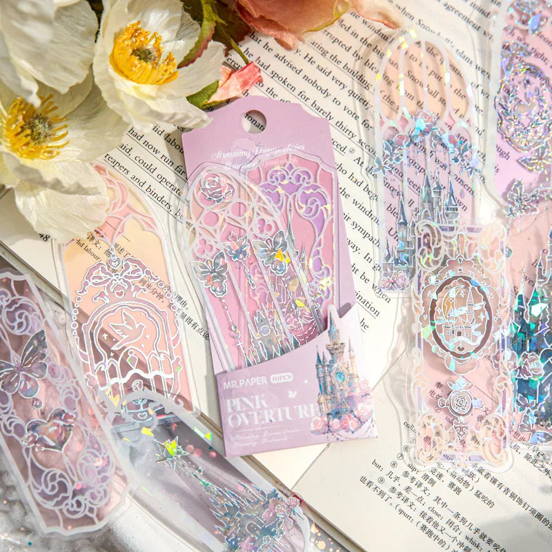 A flat-lay view of holographic fantasy bookmarks scattered over an open book and white flowers.