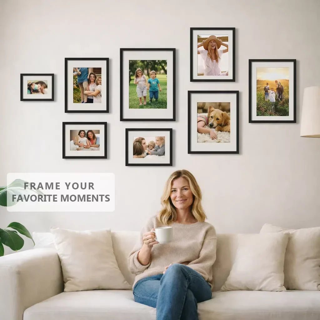 A gallery wall arrangement of multiple family photos in black frames above a sofa with a woman.