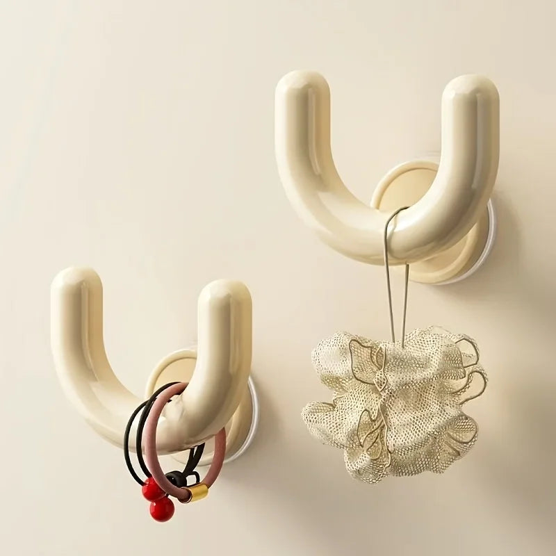 Two cream wall-mounted hooks, one holding hair ties and the other a bath sponge.