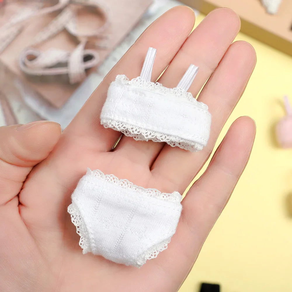 A small white lace doll bra and panty set held in a hand.