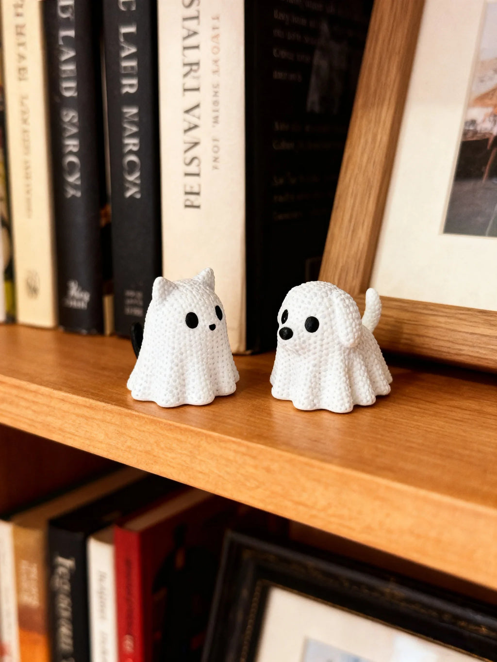 Small white ghost cat and ghost dog figurines placed on a wooden bookshelf