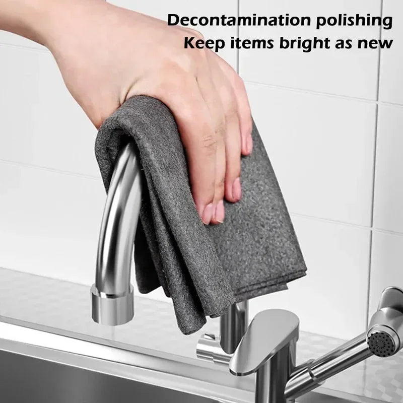 A hand using a grey microfiber cloth to polish a metal kitchen faucet.
