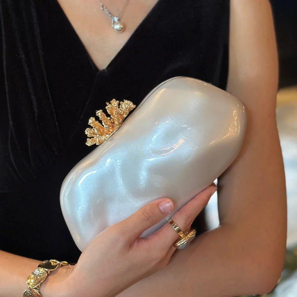 White marbled acrylic evening clutch with gold coral-shaped clasp held by a woman