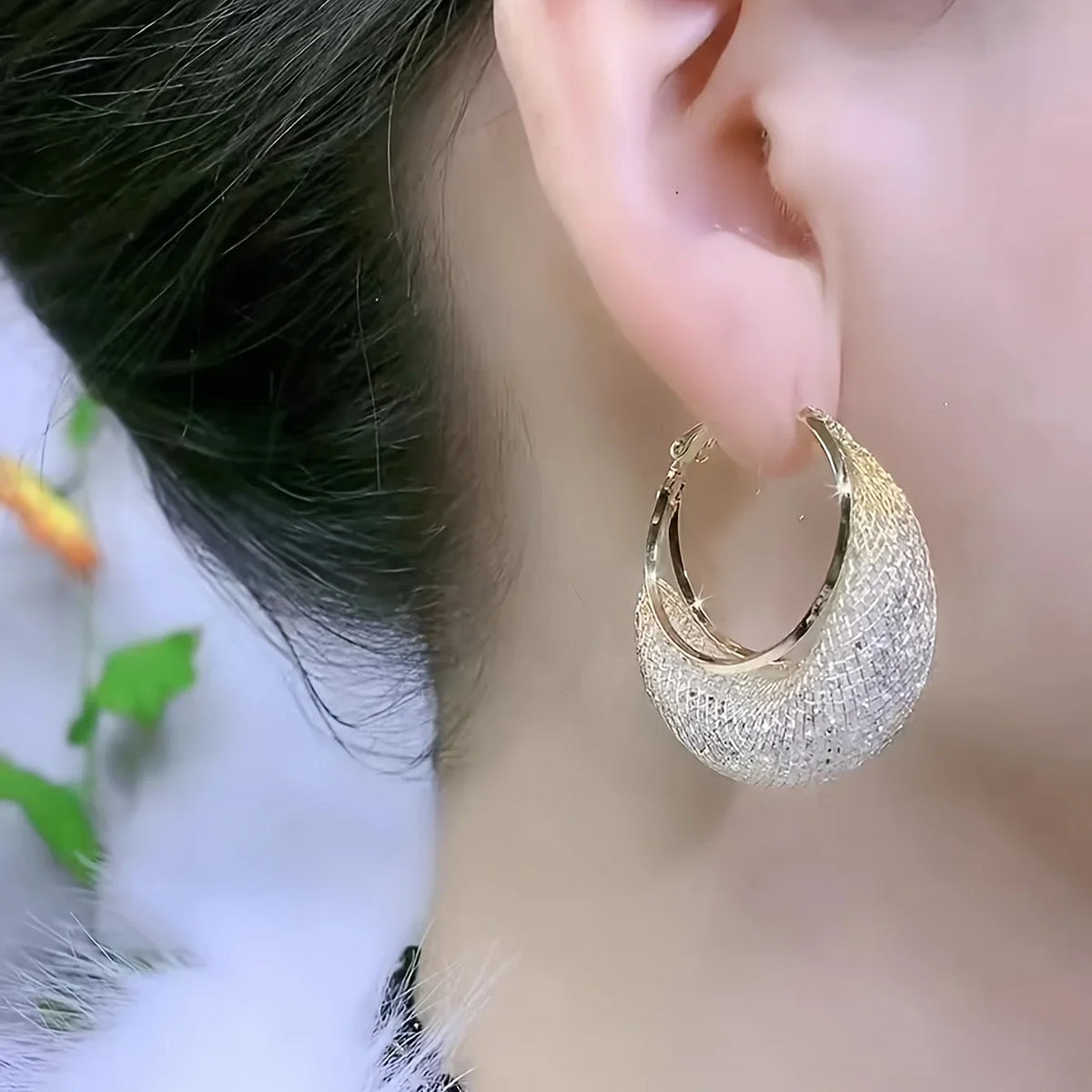 Gold-tone hoop earrings with mesh pattern and rhinestone inlay worn on an ear