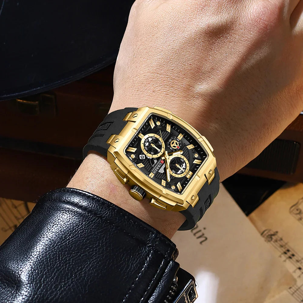 Men's square chronograph watch with gold case, black dial, and black silicone strap worn on wrist
