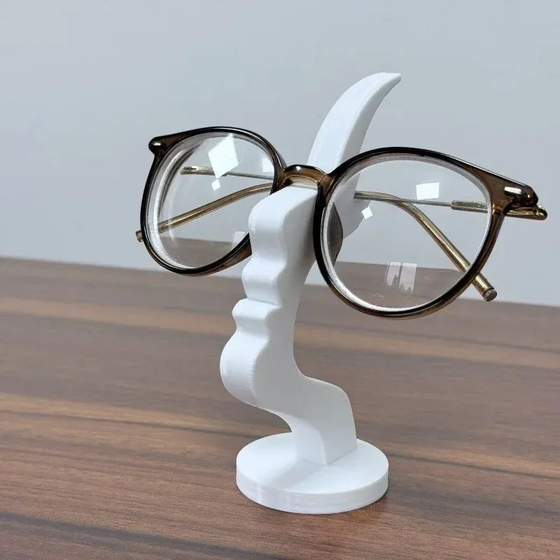 White 3D-printed minimalist human profile sculpture holding eyeglasses on a desk
