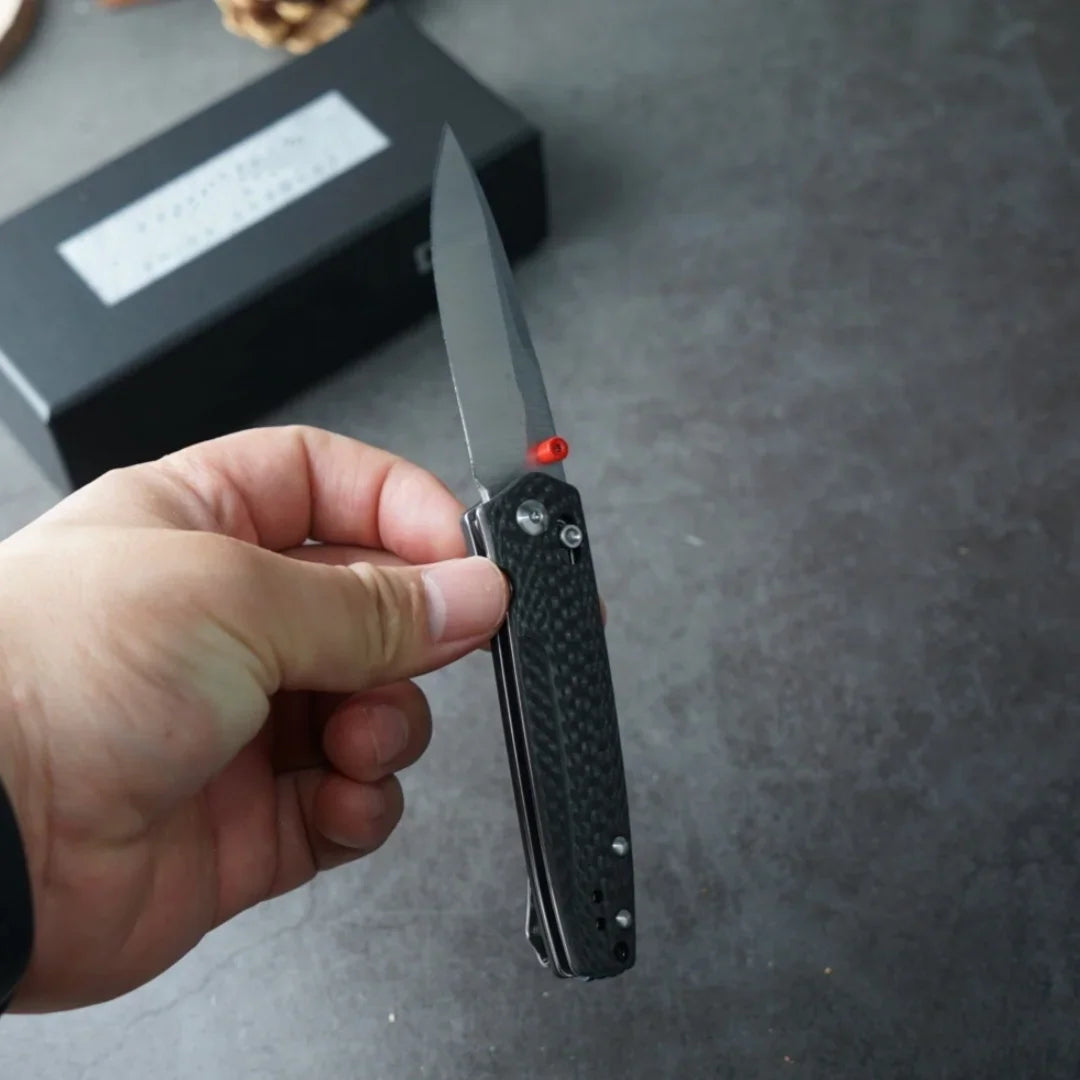 Hand holding a closed tactical folding knife with a carbon fiber handle