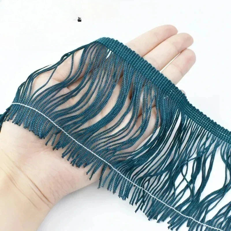 A close up of a hand holding a piece of dark green long tassel fringe trim