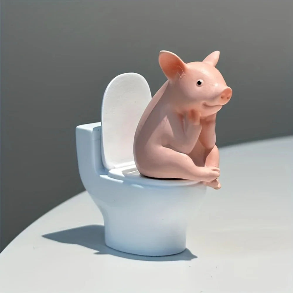 A close-up view of a cute pink pig figurine sitting on a miniature white toilet on a tabletop.