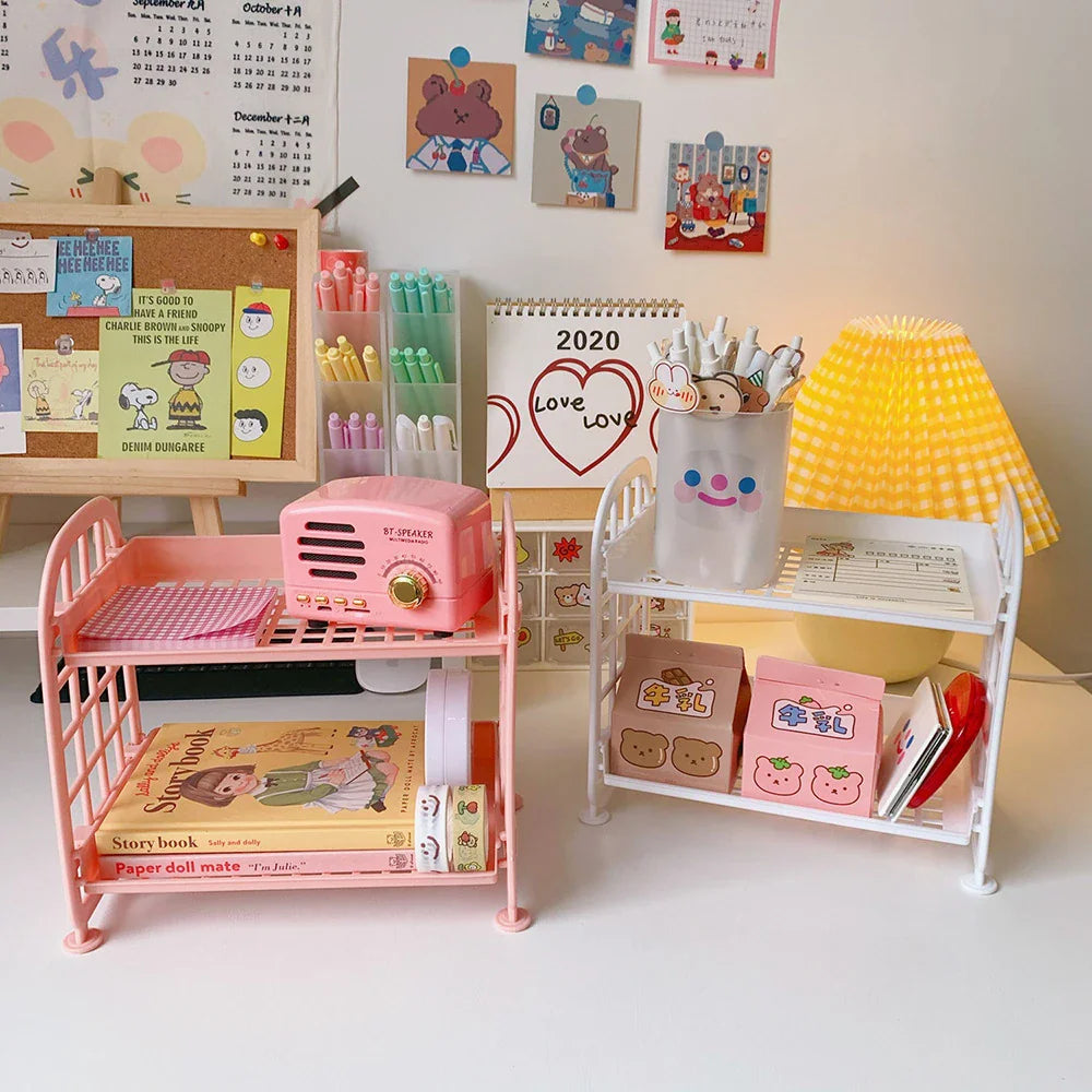 Two-tier plastic desk storage shelves in pink and white with decorative items