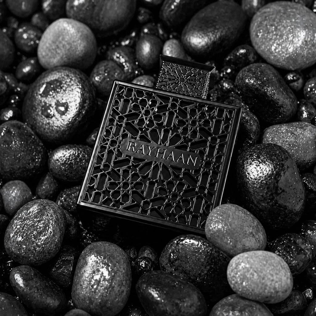 Black perfume bottle with decorative overlay placed among smooth dark river stones