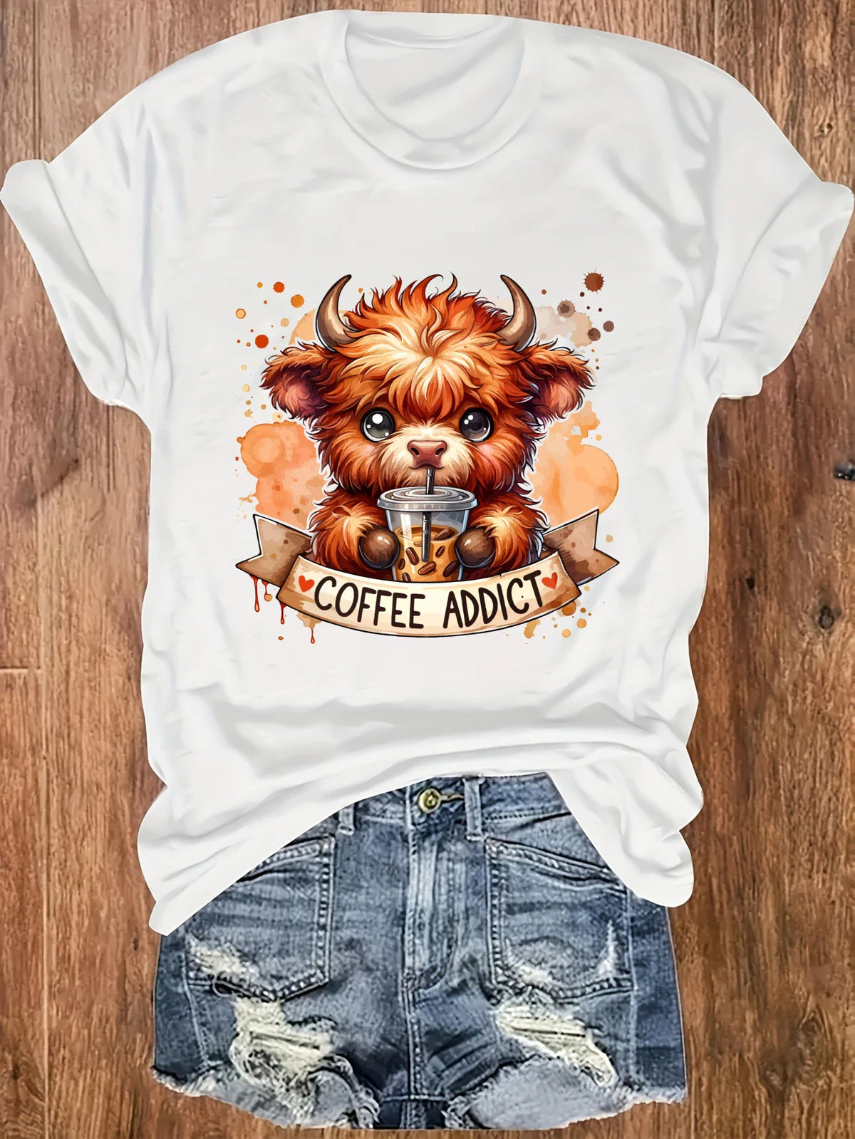 White short-sleeve t-shirt with a highland cow coffee print, worn with denim shorts.