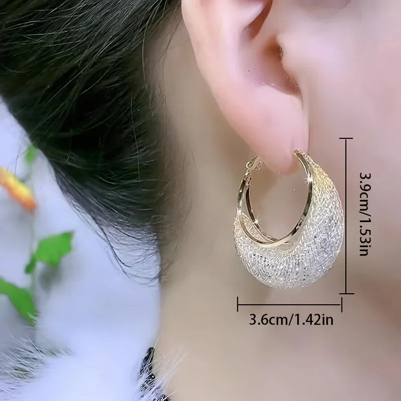 Gold hoop earrings with mesh detail and rhinestones worn on an ear
