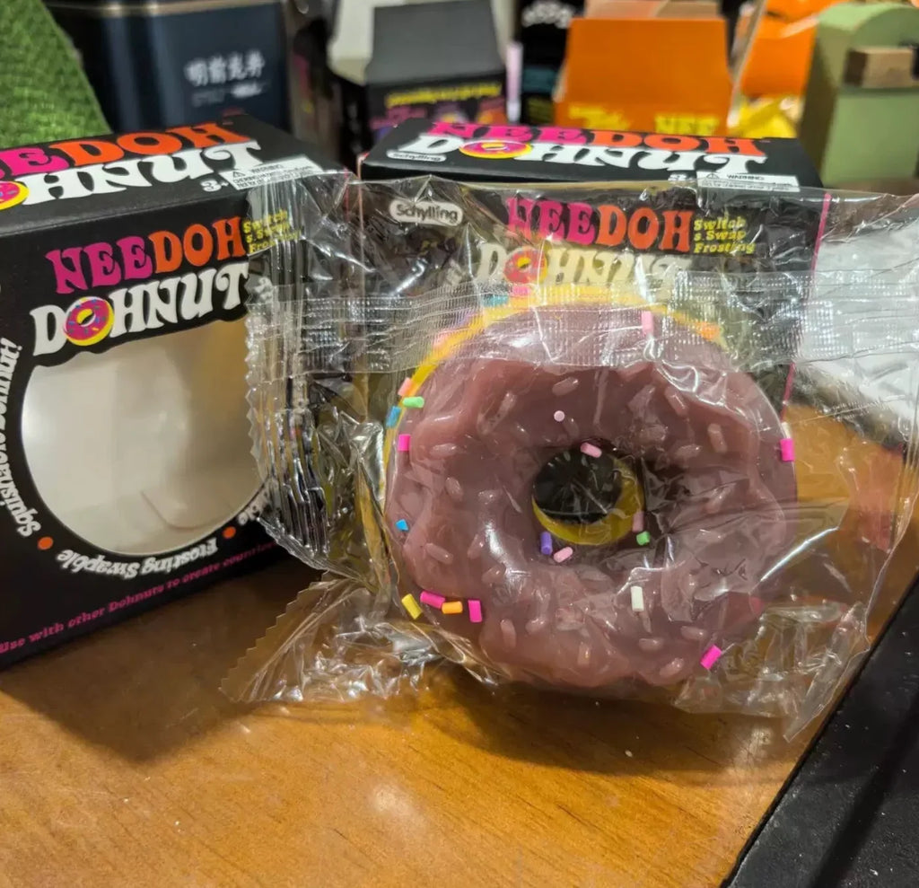 A chocolate-colored squishy donut toy in plastic packaging next to its storage box.