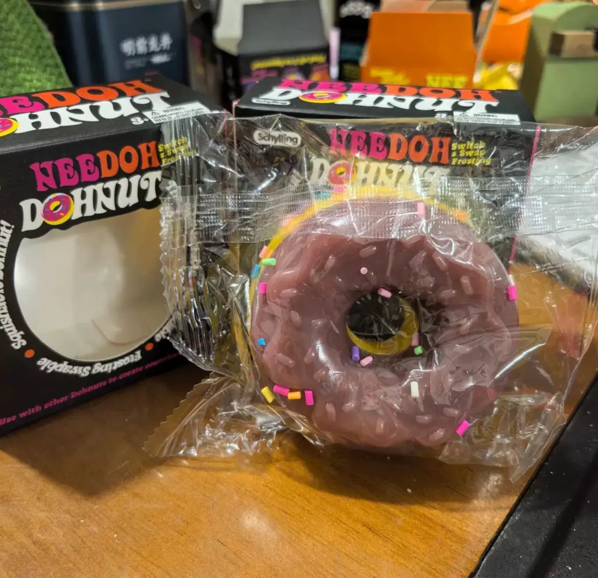 A chocolate-colored squishy donut toy in plastic packaging next to its storage box.