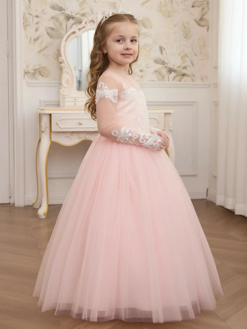 A side view of a young girl wearing a long pale pink dress with white lace appliques and sheer long sleeves.