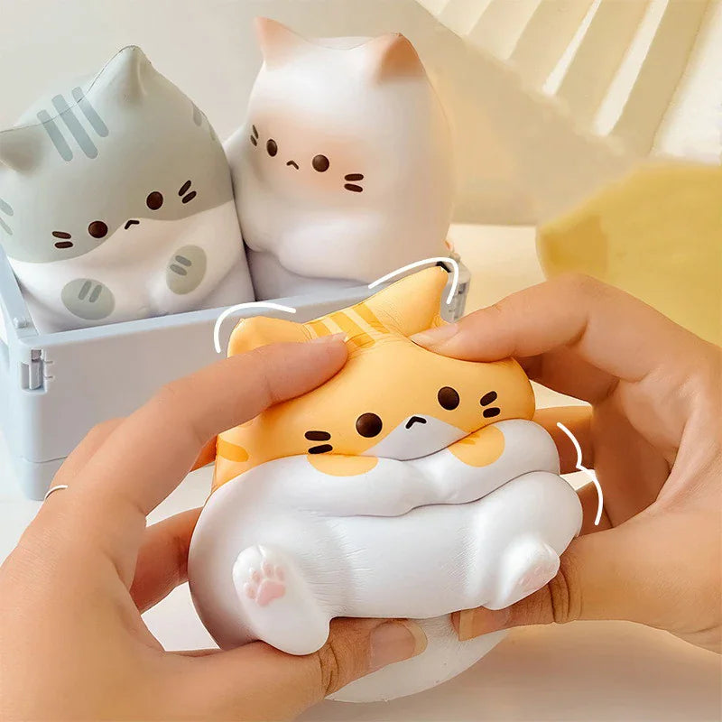 A hand squeezing a yellow and white cartoon cat-shaped stress relief toy.