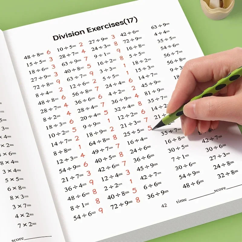 A hand using a green pen to complete a page of division exercises in a workbook.