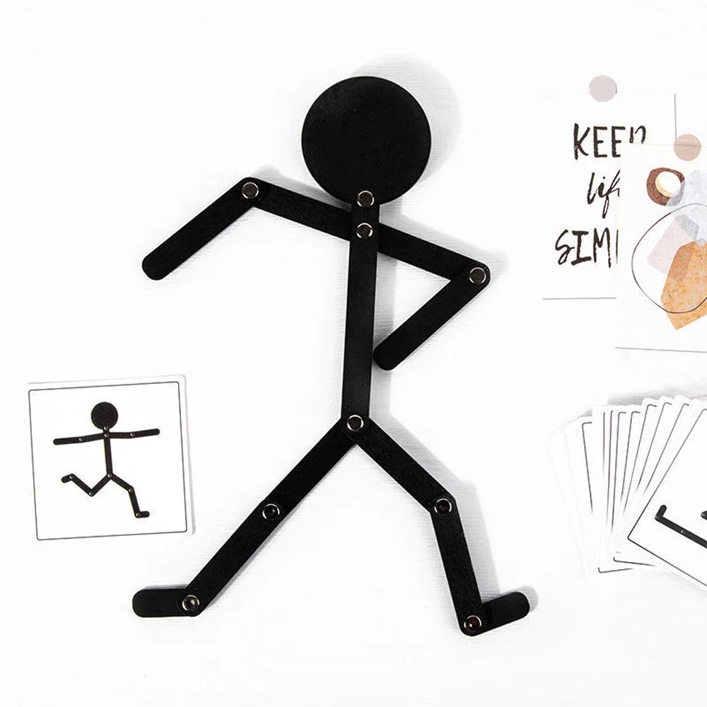 A black articulated wooden stick figure toy displayed next to a reference card and a decorative note.