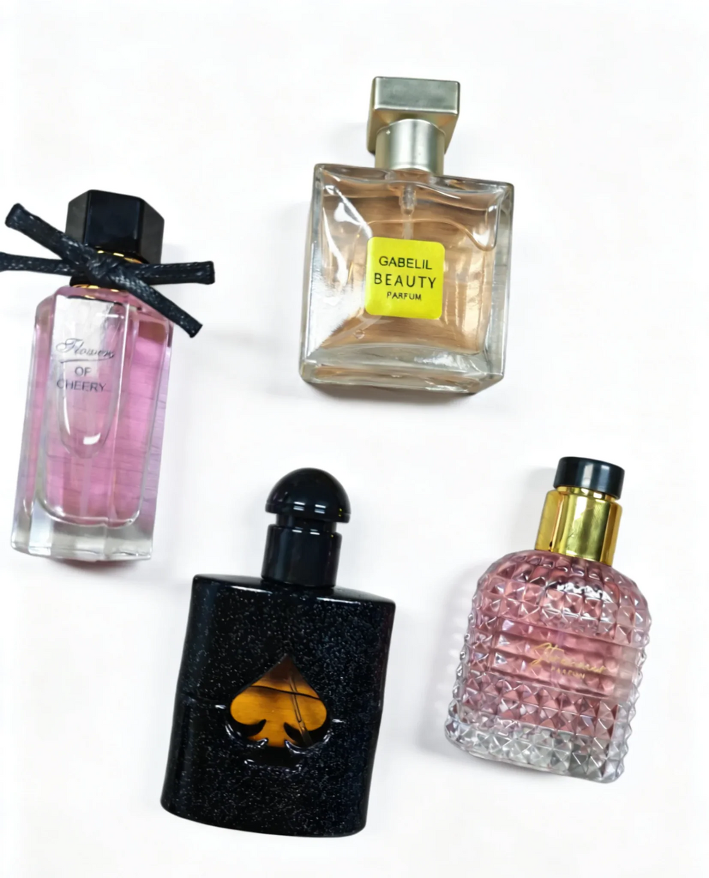 A group of four distinct perfume bottles, one tall with a bow, one square, one black spade-shaped, and one textured pink.