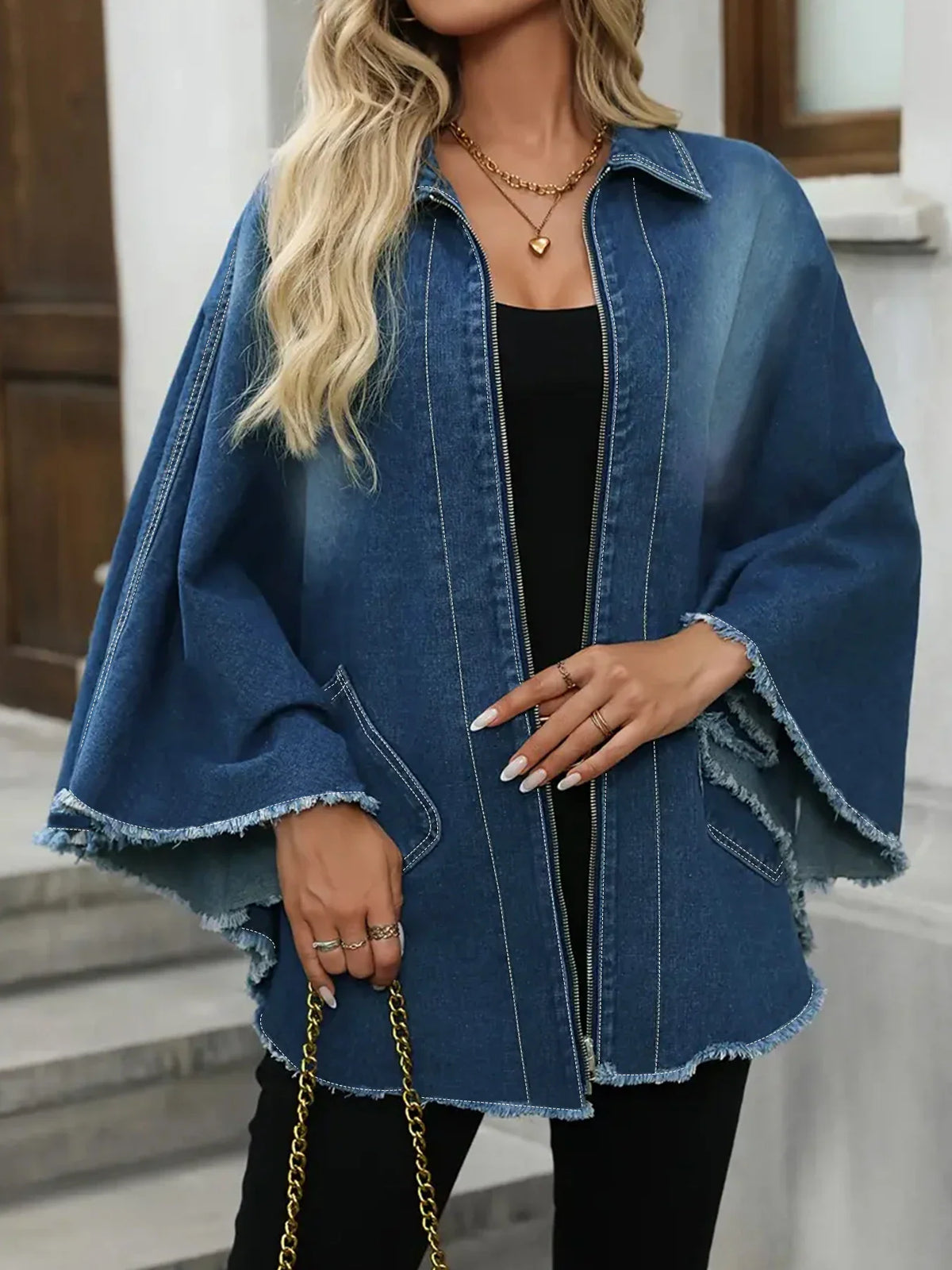 A woman showcasing a blue denim cloak-style jacket with a frayed hem, styled with a gold chain bag
