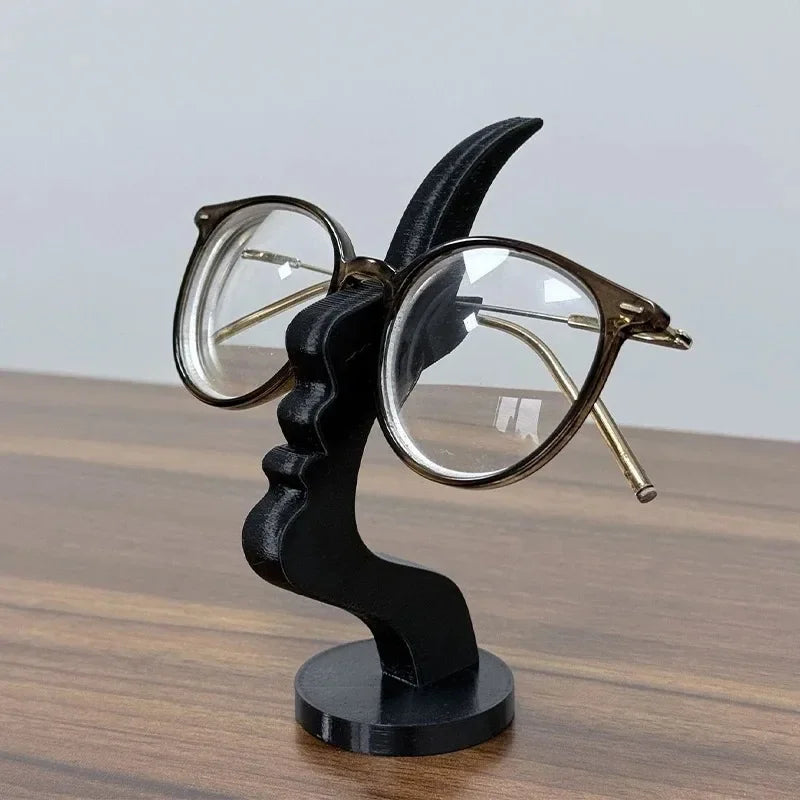 Minimalist black 3D-printed human profile sculpture holding eyeglasses on a desk