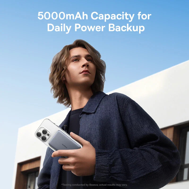 A young man holding a smartphone with an attached magnetic power bank against a clear sky background.