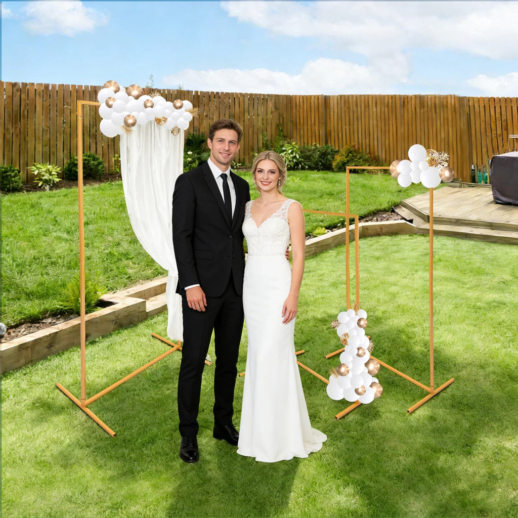 Gold metal wedding arch display stands decorated with balloons and fabric in a garden