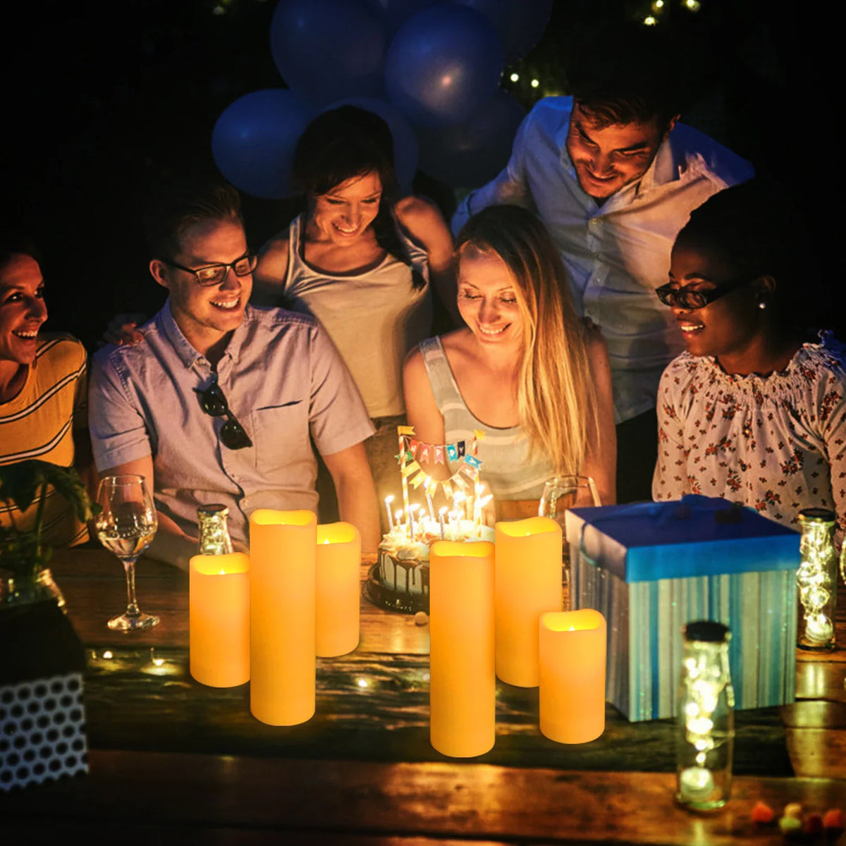 Group of friends celebrating a birthday with many glowing LED pillar candles on the table.