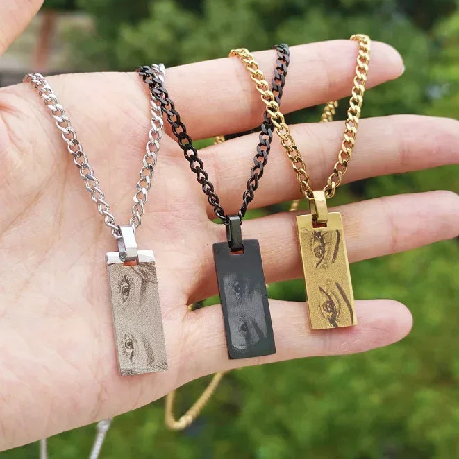 Hand holding three personalized photo engraved bar necklaces in silver, black, and gold tones.