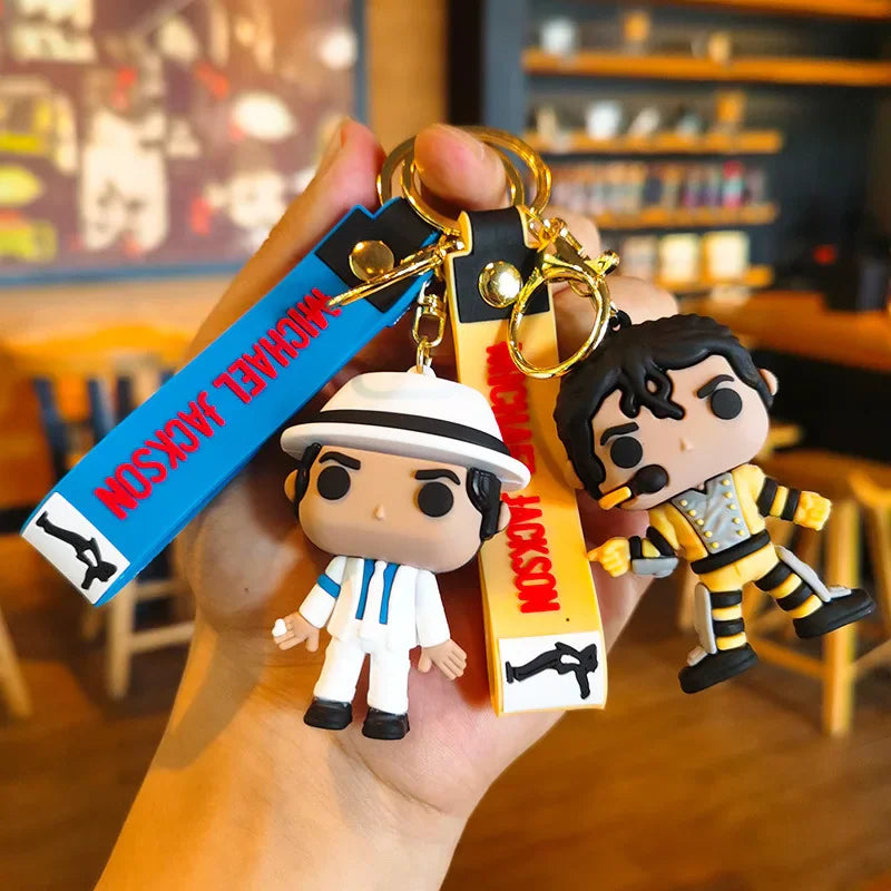 Hand holding two Michael Jackson vinyl-style doll keychains, one in a white suit, one in a yellow jacket.