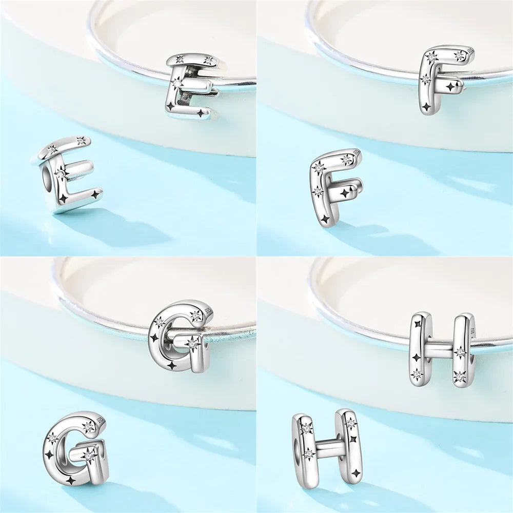Sterling silver letter charms E, F, G, H with star designs displayed on a light blue surface and a bracelet.