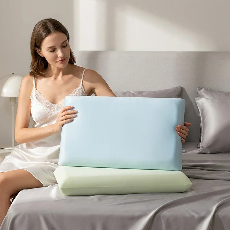 A woman holding blue and green cooling pillowcases while sitting on a bed