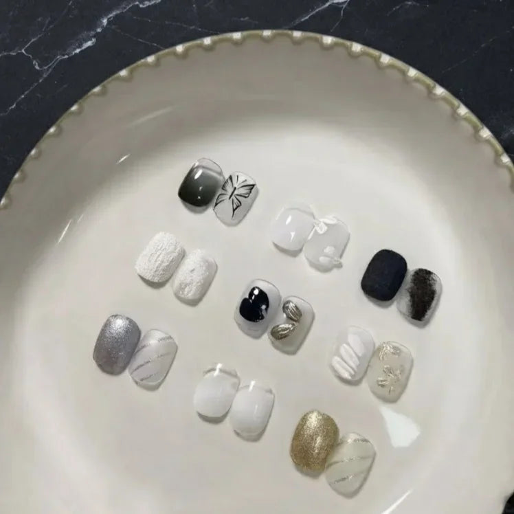 A collection of various nail art tips with black, white, and gold designs displayed on a circular plate.