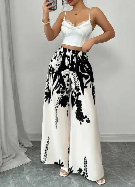 Woman wearing black and white floral print wide leg trousers with a white lace-trimmed crop top