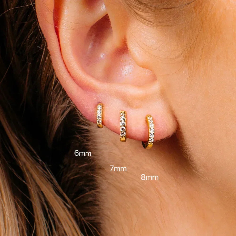 Three gold hoop earrings of different sizes worn in an ear lobe piercing.