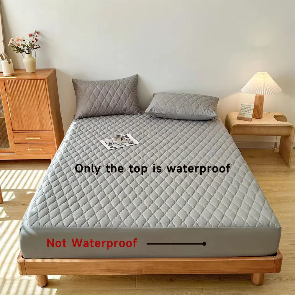 A grey quilted fitted mattress protector on a bed with text indicating the waterproof top and non-waterproof sides