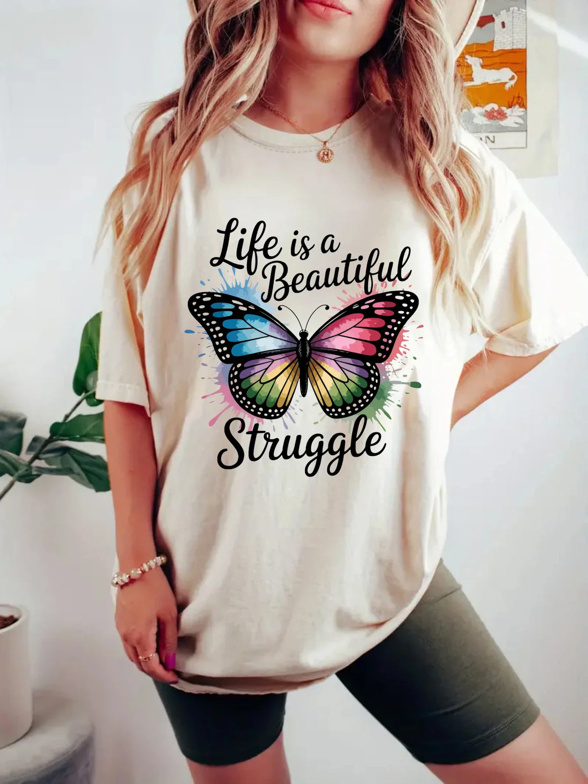 Woman wearing a beige t-shirt with a colorful butterfly graphic and the text Life is a Beautiful Struggle