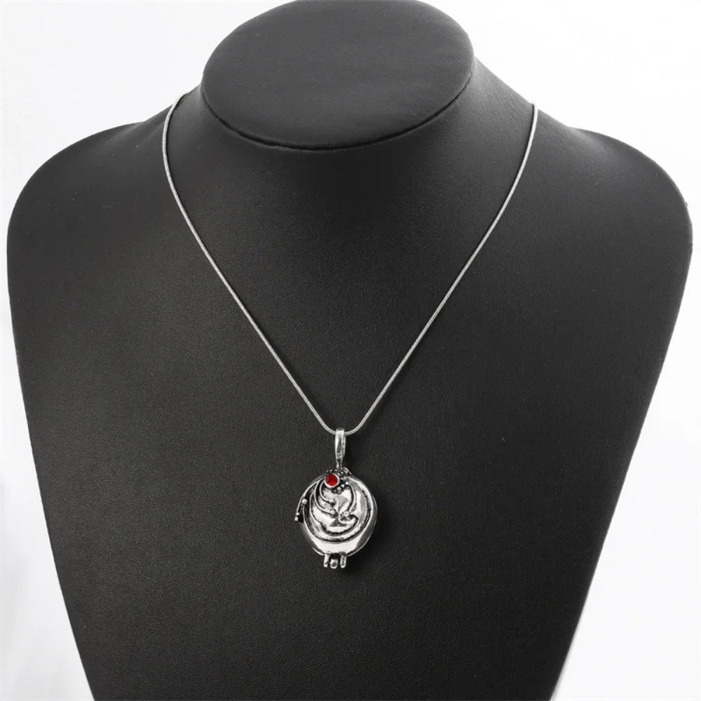 A silver locket necklace with a red gem pendant on a black bust display.