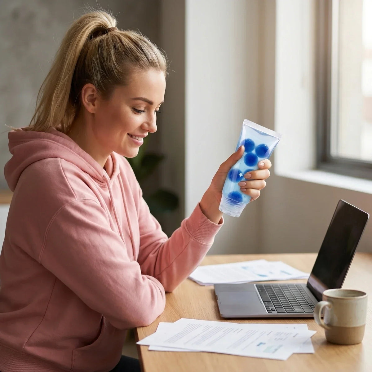 A woman holding a blue squishy toothpaste toy while sitting at a laptop.