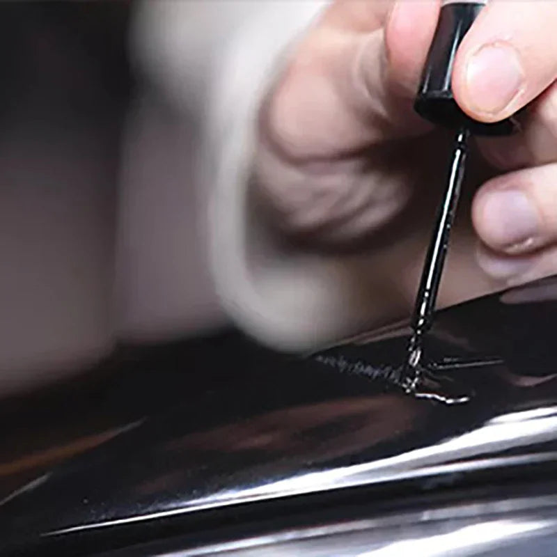 Close-up of a brush applying black touch-up paint to a car wheel scratch