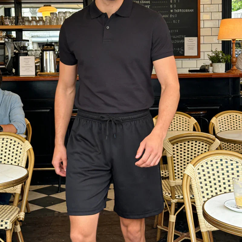 Man wearing a black polo shirt and black drawstring shorts sitting in a cafe