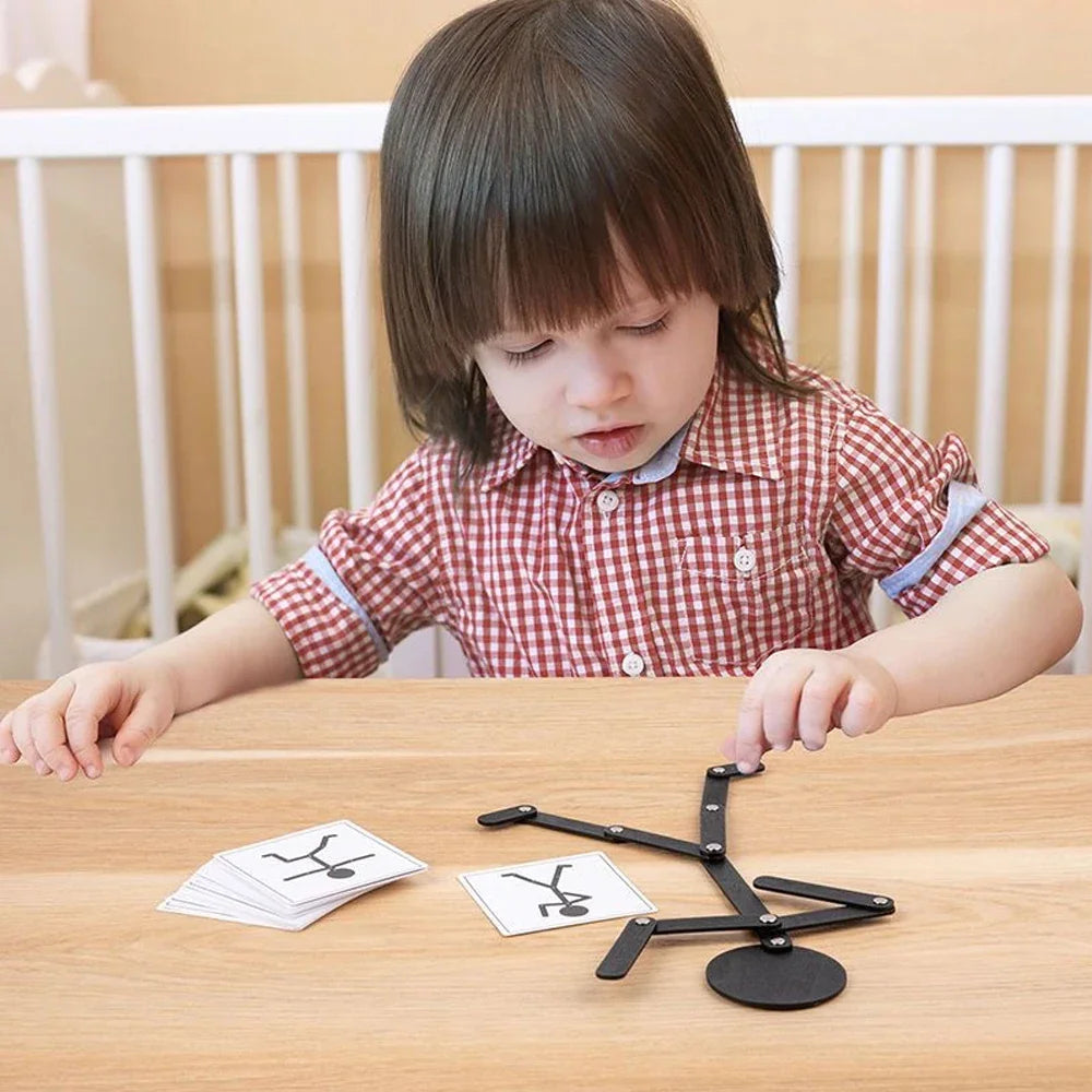A young child sitting at a table playing with a black posable wooden stick figure toy and prompt cards.
