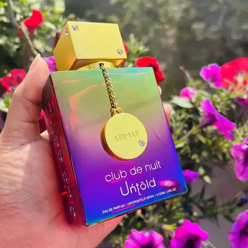 Iridescent perfume bottle held in hand in front of purple and red flowers