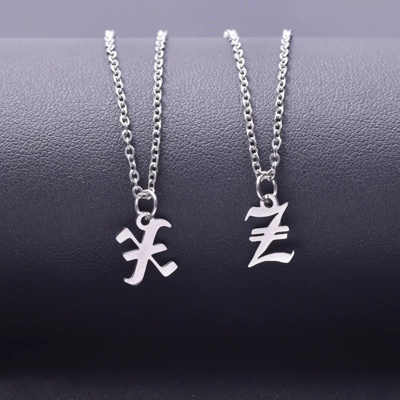 Two silver initial pendant necklaces with chain on a textured dark background